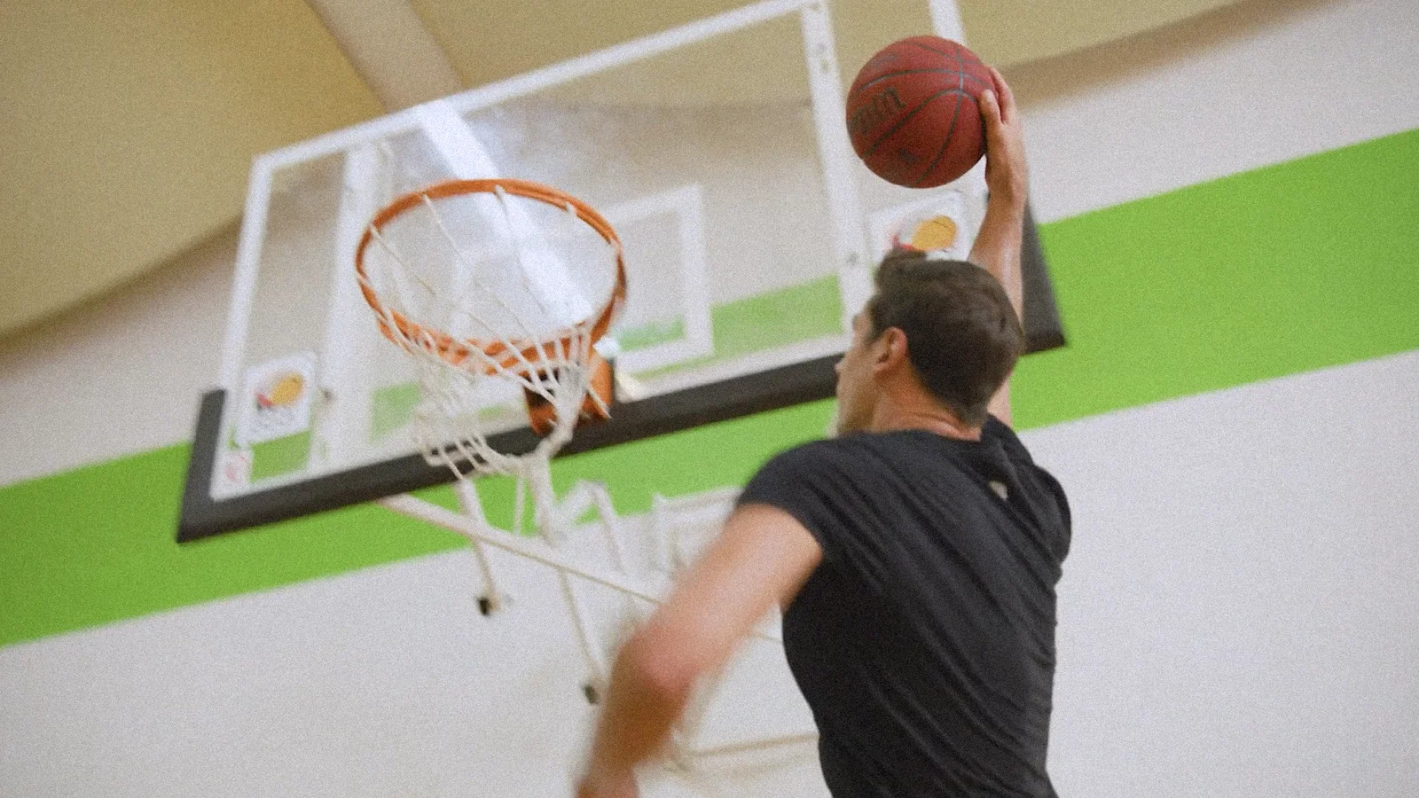 Athlete mid-air reaches for a slam dunk on an indoor basketball court