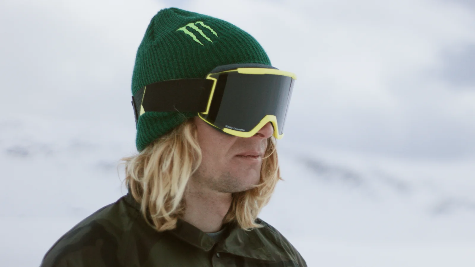 Close up of the snowboarder Simon Gruber wearing a beanie and goggles on a mountain covered in snow 