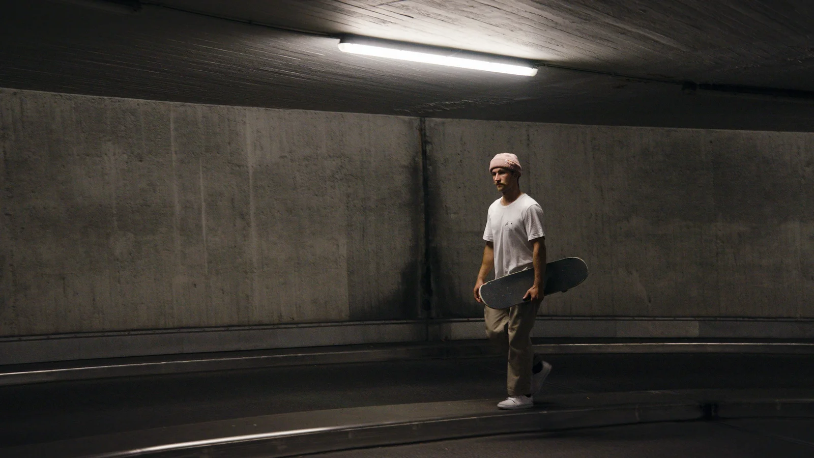 Felix Georgii carrying a skateboard in an underground carpark