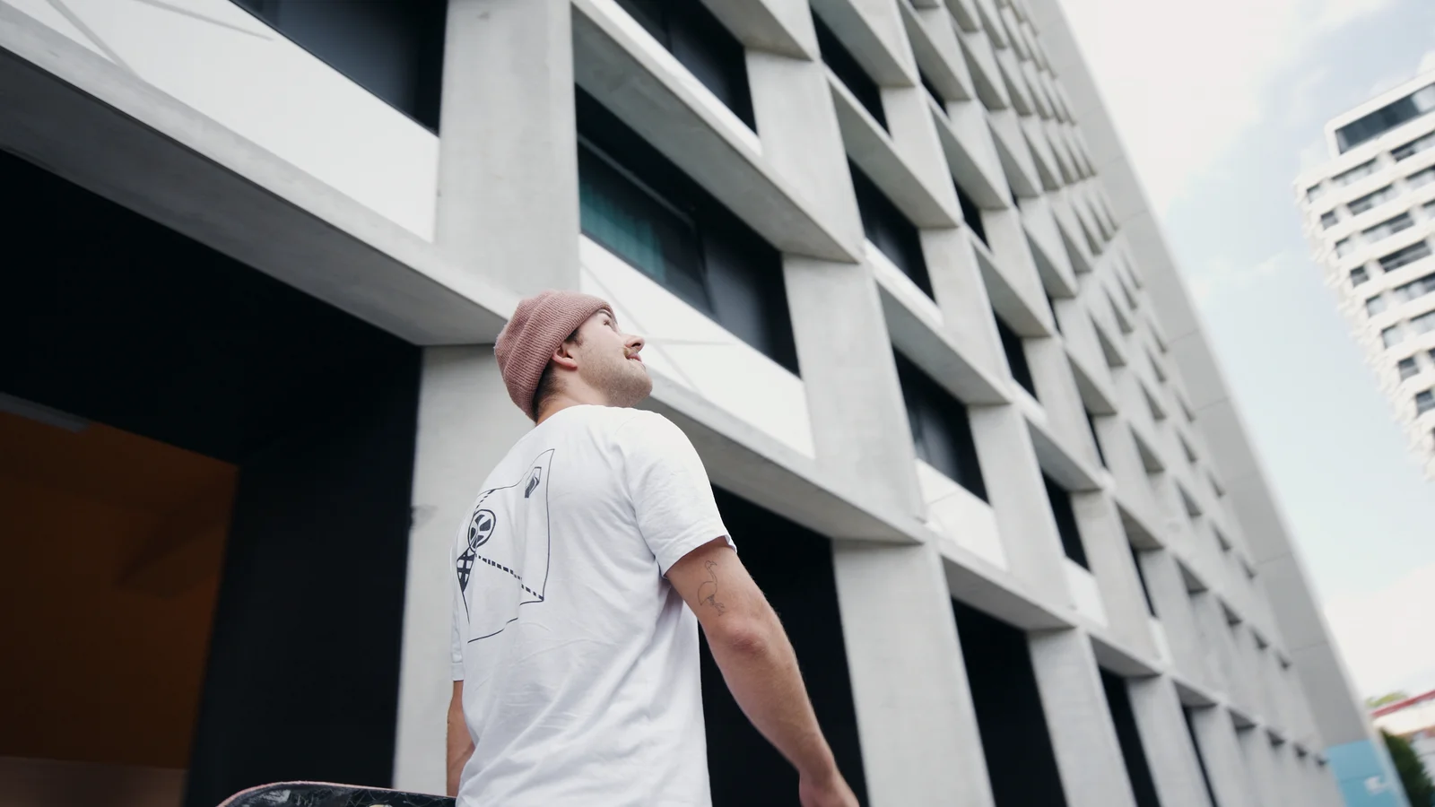Felix Georii carrying a skateboard next to modern architecture
